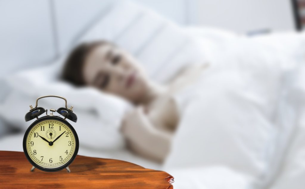 目覚まし時計の横で寝ている若い女性
