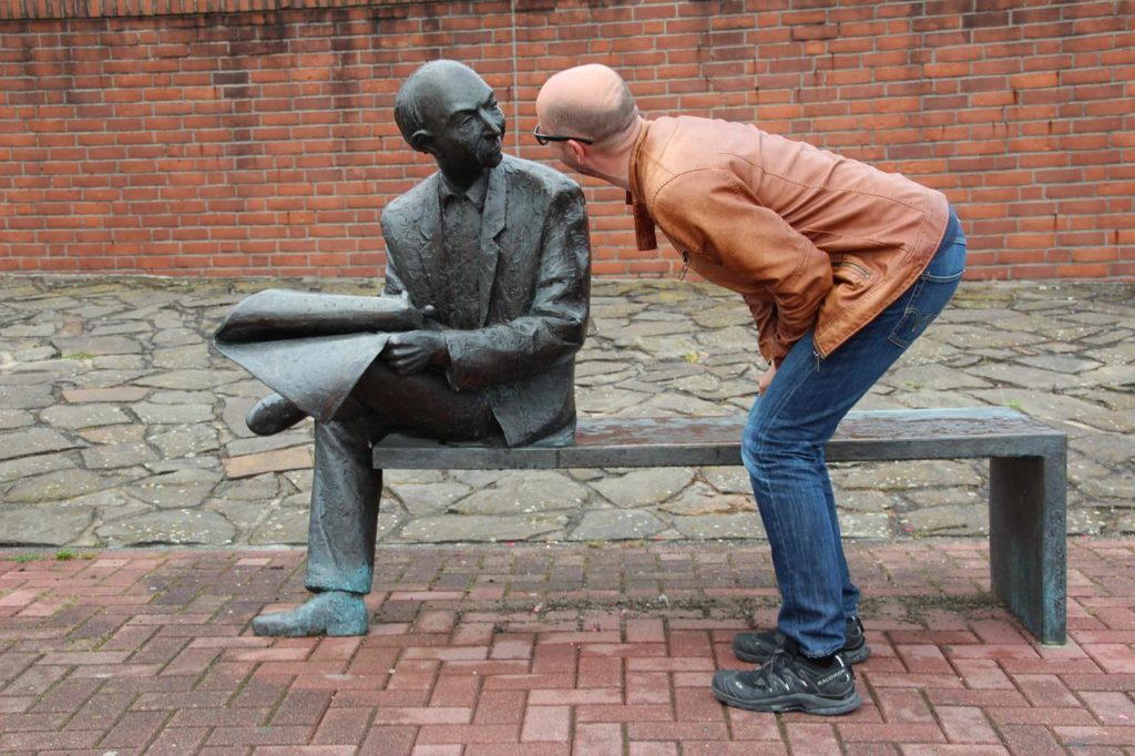 新聞を読む銅像に顔を近づける男性