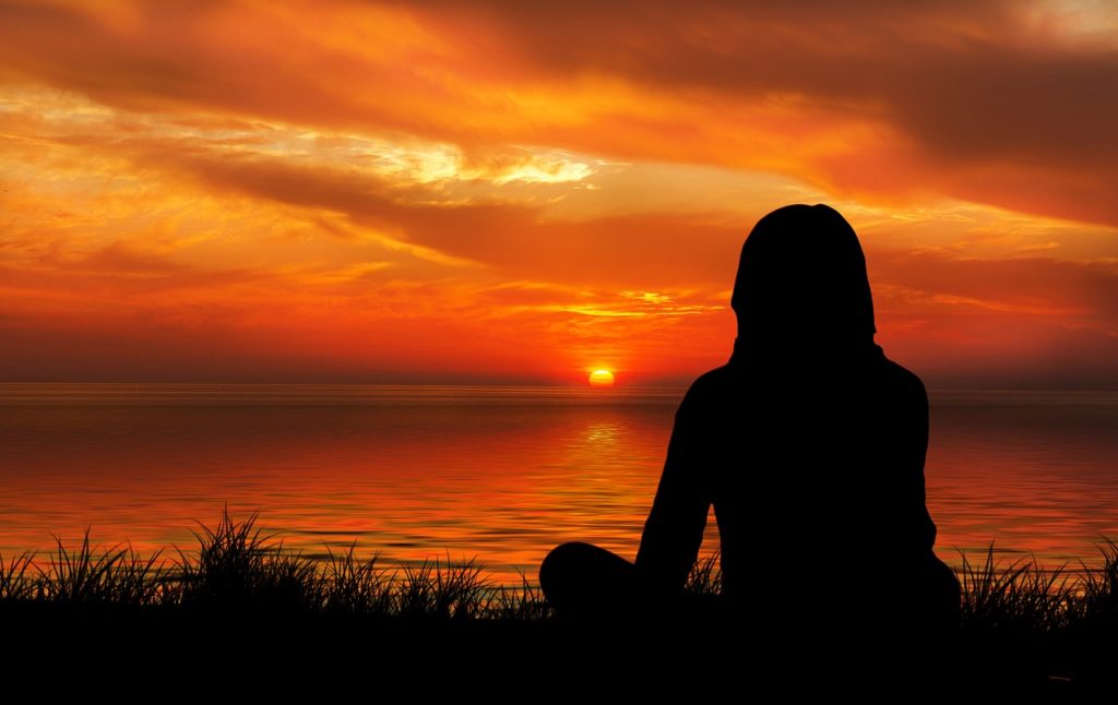 沈む真っ赤な夕日を座って眺める女性の影