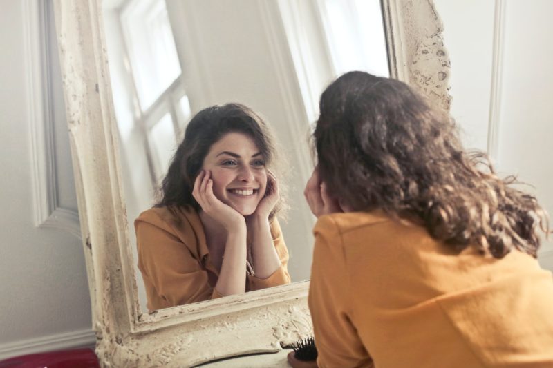 鏡を見て笑顔を作る黄色い服の女性