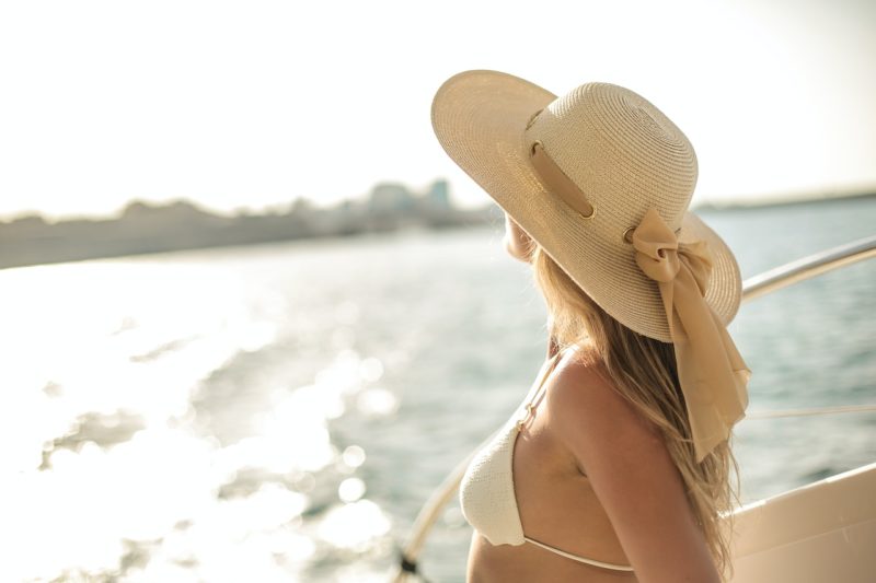 開放的な船の上で水着を着て海を眺める帽子をかぶった女性