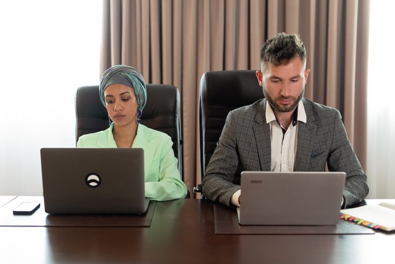 机に座りノートパソコンをする男女