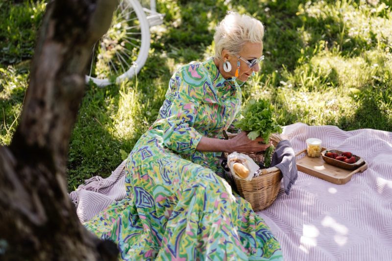 外の芝生でランチを食べるおしゃれなおばさん