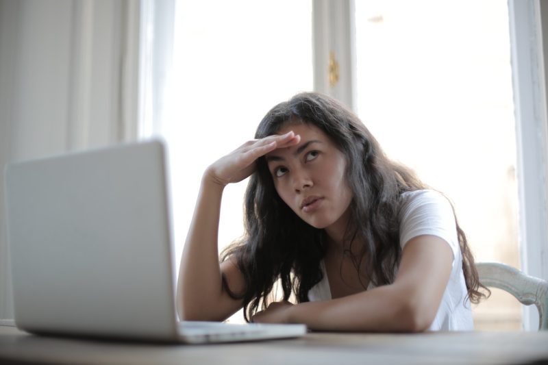ノートパソコンの前で頭を抱える白いＴシャツの女性