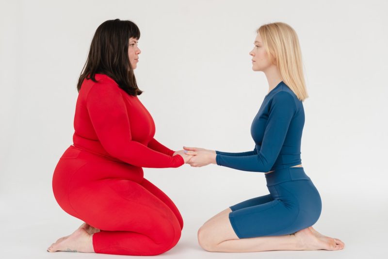 赤のタイツの太った女の人と青のタイツの痩せた女の人が手を合わせている