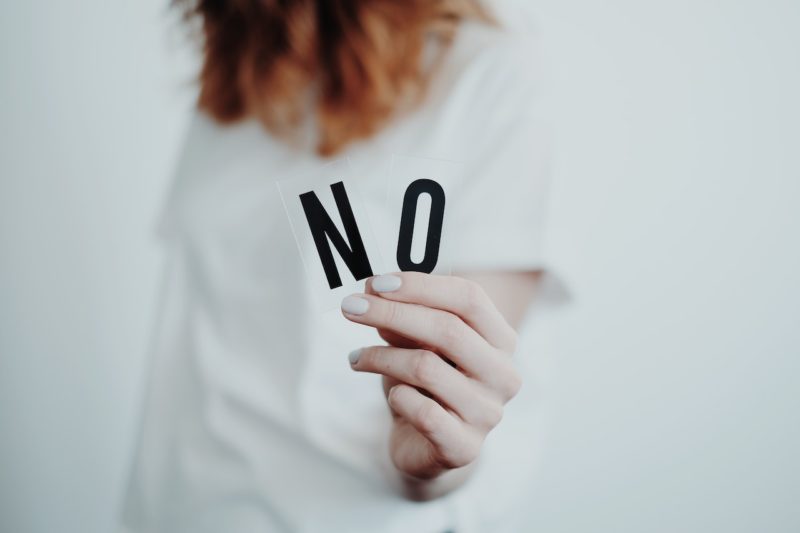 「NO」という文字をこちらに向ける女性