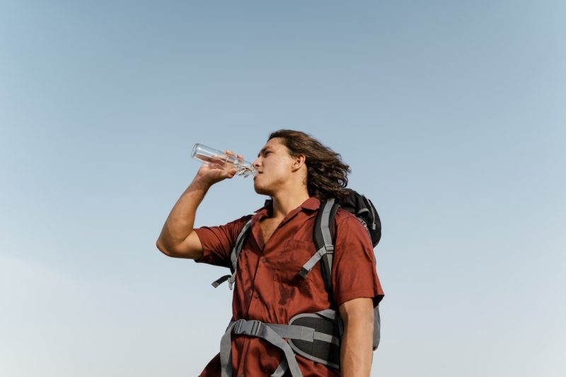バックパックを背負ってペットボトルの水を飲む男性