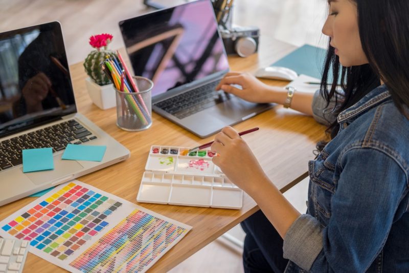 ノートパソコンを操作しながらパレットで色を選ぶ女性