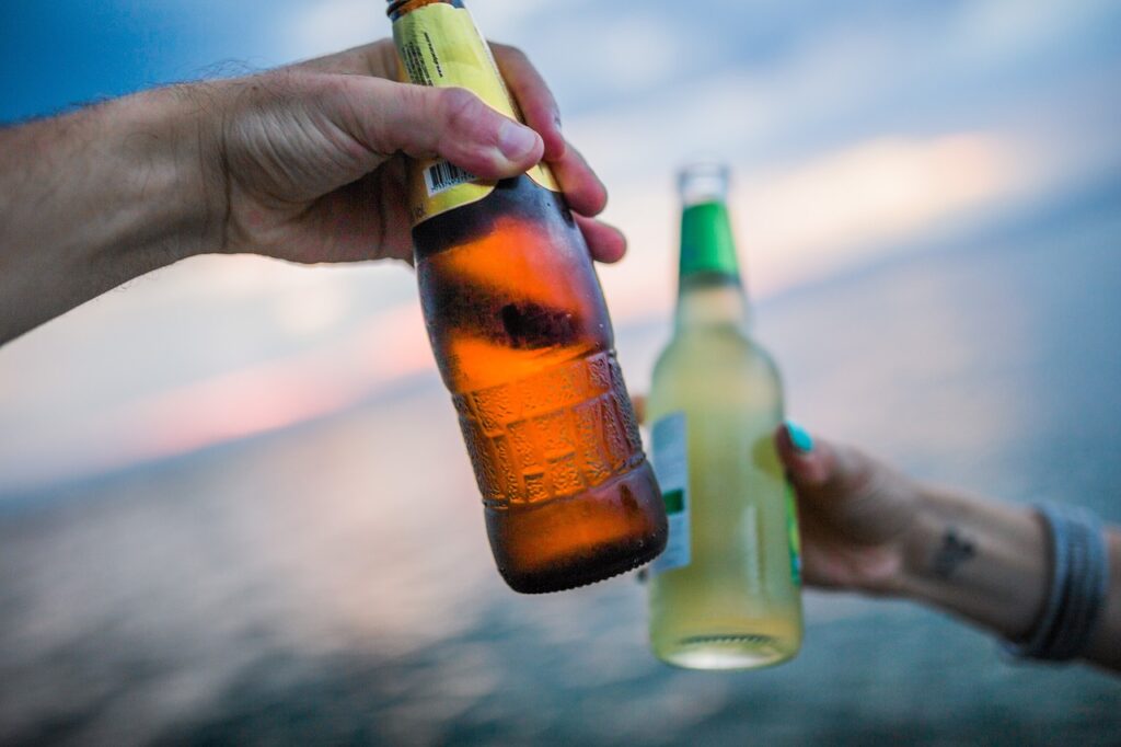 海で仲良くお酒の瓶で乾杯する手元