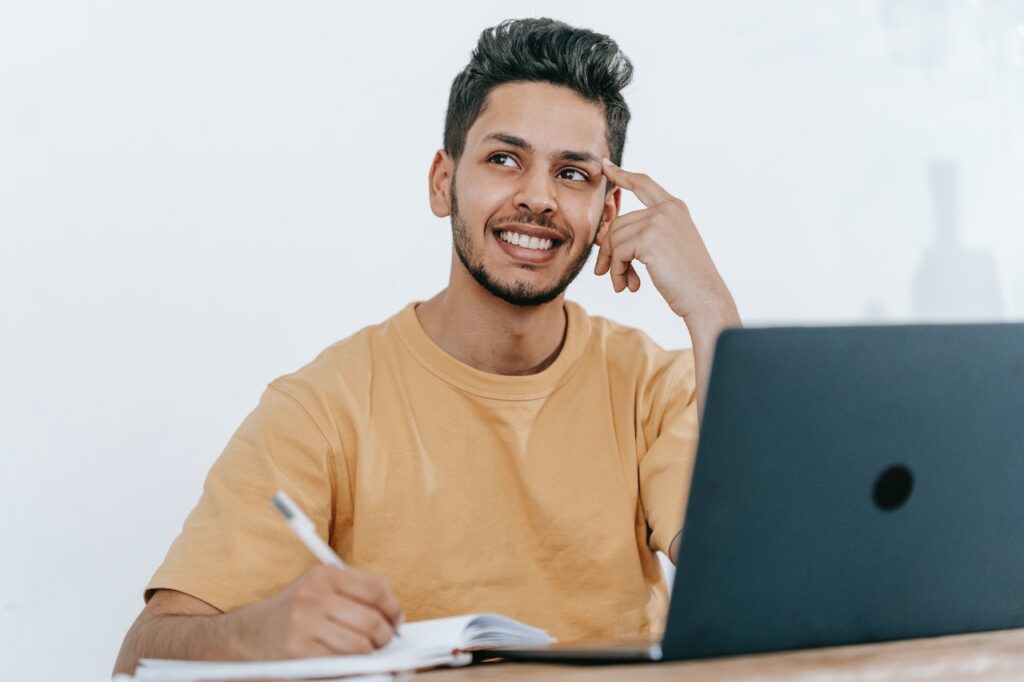 ノートパソコンの前で笑顔で何かを考えている男性