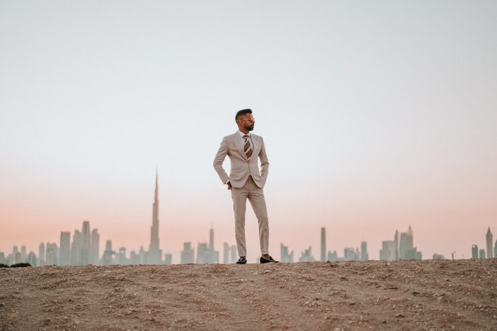 高層ビルを背にして砂の上で立っているスーツの男