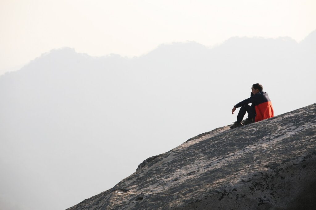 山の斜面に1人で座っている寂しげな男性