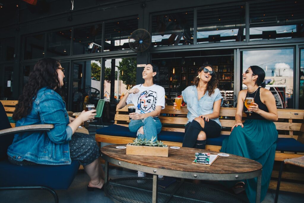 友達たちとカフェの外でビールを飲んで談笑している女性