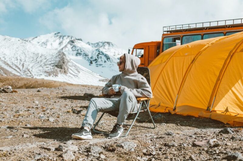 雪山の上にテントを張って一人で何かを飲んでいる男性