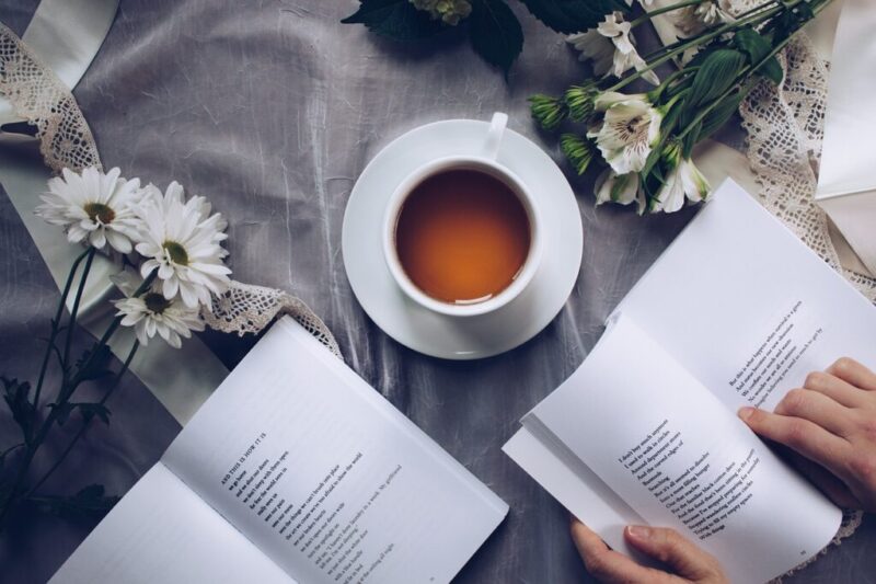 紅茶と花をテーブルに並べて本を読んでいる様子